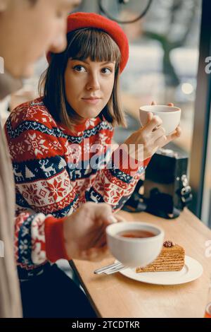 Nachdenkliche junge Dame in einem Weihnachtspullover, die Tee in einem malerischen Café schmeckt Stockfoto