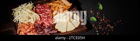 Banner mit Wurstplatte mit Gourmet-Käseauswahl, getrocknetem Rindfleisch und Salamischeiben auf Schwarz Stockfoto