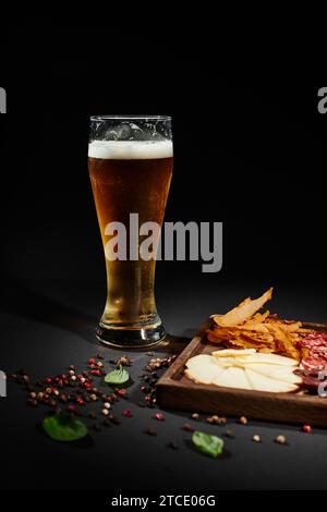 Ein Glas Craft-Bier in der Nähe der Wurstplatte mit Gourmet-Käse, getrocknetem Rindfleisch und Salami auf Schwarz Stockfoto