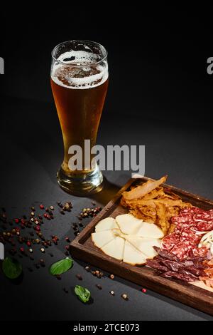 Ein Glas Craft-Bier in der Nähe der Wurstplatte mit Gourmet-Käse, getrocknetem Rindfleisch und Salami an Bord Stockfoto