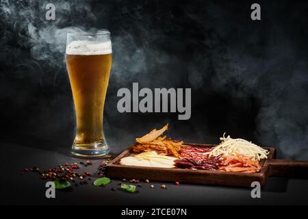 Ein Glas Craft-Bier in der Nähe der Wurstplatte mit Käseauswahl, getrocknetem Rindfleisch und Salami auf Schwarz Stockfoto