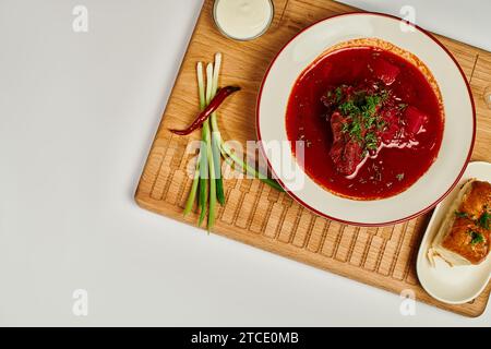 Traditioneller ukrainischer Borsch mit frischem Dill in der Nähe von Knoblauchbrötchen und Sauerrahm auf Schneidebrett Stockfoto