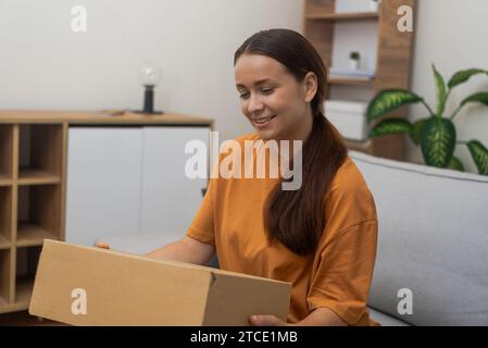 Frau, die riesige Pappschachtel aus dem Internet-Shop auspackt und sich aufgeregt hat, das Paket zu erhalten Stockfoto