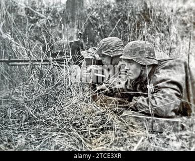 DEUTSCHE WAFFEN-SS-Soldaten feuern ein leichtes Maschinengewehr MG26 mit Tarnhelmen und Mänteln ab. Stockfoto