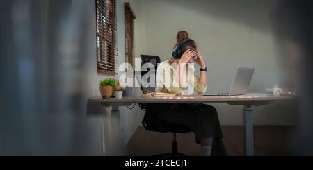 Asiatische Frauen sind gestresst, während sie am Laptop arbeiten, müde asiatische Geschäftsfrau mit Kopfschmerzen im Büro fühlt sich krank an der Arbeit Stockfoto