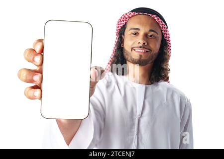 Junger arabischer Mann in traditioneller Kleidung, der Smartphone mit leerem Bildschirm auf weißem Hintergrund zeigt Stockfoto