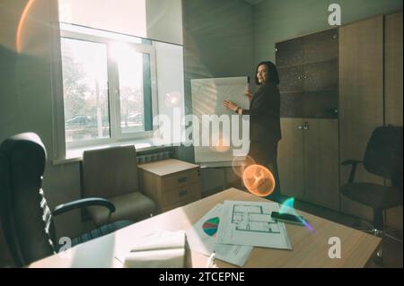 Glückliche Geschäftsfrau im Büro. Eine Tutorin oder Trainerin vor dem Brett im Sonnenlicht Stockfoto