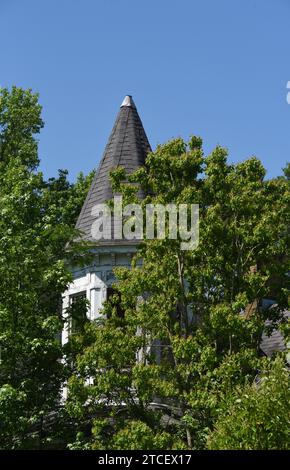 Altes, historisches, viktorianisches Haus wurde überwuchert und verlassen. Der runde Turm ist mit einer Zinnkappe und Schindeln gekrönt. Die Farbe ist rissig und blättert ab. Stockfoto