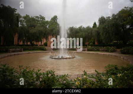 Ein kreisförmiger Brunnen ist das Herzstück einer ruhigen, landschaftlich gestalteten Gegend. Der Brunnen schießt einen hohen, kräftigen Wasserstrahl in die Luft und erzeugt einen Nebel. Stockfoto