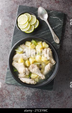 Bahama Chicken Souse mit Hähnchenflügel, Kartoffeln, Sellerie, Limette und Gewürzen aus der Nähe auf dem Teller auf dem Tisch. Vertikale Draufsicht von oben Stockfoto