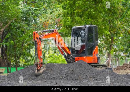 Der orangefarbene Minibagger im Betrieb gräbt und lädt fruchtbaren Boden im Park Stockfoto