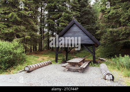 Ein traditioneller Picknicktisch aus Holz, komplett mit Bänken im Schatten einer rustikalen Holzunterkunft. Stockfoto