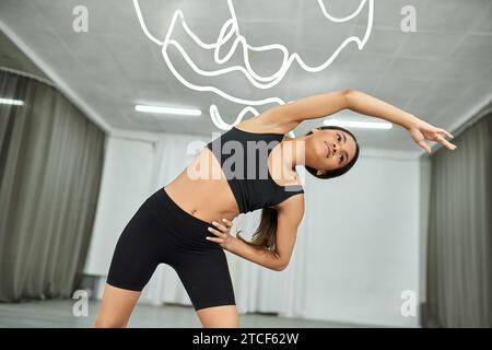 Flexible afroamerikanische Tänzerin in schwarzer Sportbekleidung, die beim Training im Studio seitliche Lounges macht Stockfoto