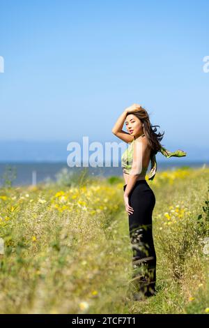 Schöne junge asiatische Frau kurvige Figur athletisch stehend in einer blühenden Feldbucht an einem windigen Frühlingstag Stockfoto