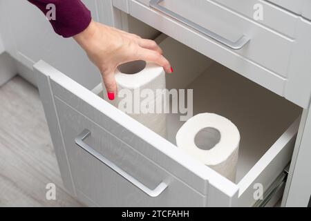 Frau, die Papierhandtuch aus der Küchenschublade herausnimmt. Die Hand nimmt ein Papiertuch heraus. Papiertuch in der Küche Stockfoto