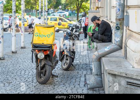 Bukarest, Rumänien - 17. August 2023: Glovo-Kurier für Lebensmittellieferungen überprüft sein Telefon auf Bestellungen in der Altstadt von Bukarest. Stockfoto
