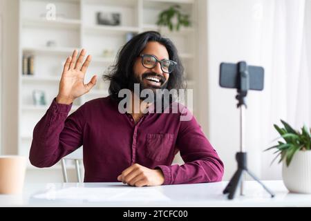 Fröhlicher indischer Freelancer, der während eines Live-Streams oder Videoanrufs hallo winkt Stockfoto