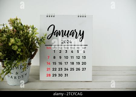 Monatskalender Januar 2024 mit grüner künstlicher Pflanze in Metallvase auf hölzernem Hintergrund Stockfoto