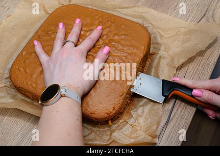 Zubereitung von polnischem Kuchen, Fudge mit Vanillecreme, Frau schneidet den Kuchen in zwei Teile. Stockfoto