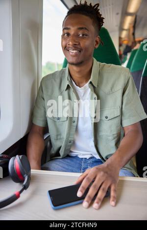 Porträt Eines Jungen Mannes, Der Mit Schnurlosen Kopfhörern Und Mobiltelefon Im Zug Zur Arbeit Fährt Stockfoto