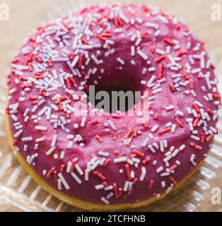 Ein Blick aus der Nähe auf einen köstlichen rosa Donut mit bunten Streuseln, eine köstliche Dessert- oder Snackoption, vor einem weißen Hintergrund Stockfoto