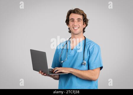 Gesundheitswesen und Telemedizin. Lächelnder männlicher Arzt mit blauem Uniformmantel und Stethoskop, der Laptop hält Stockfoto