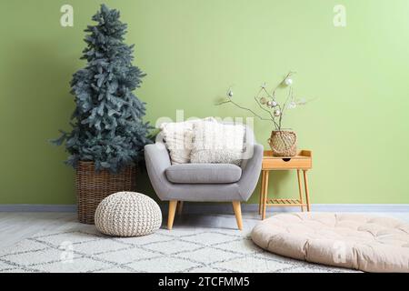 Innenraum des festlichen Wohnzimmers mit Weihnachtsbaum, grauem Sessel und Hocker in der Nähe der grünen Wand Stockfoto