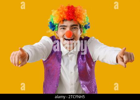 Glücklicher junger Mann im Clown-Kostüm, der auf den Zuschauer auf gelbem Hintergrund zeigt Stockfoto