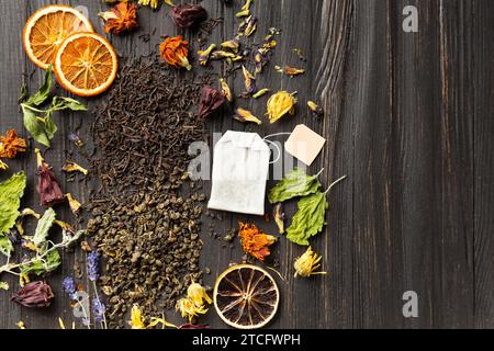 Zusammensetzung von trockenem schwarzem und grünem Tee, Teebeutel, getrockneten Zitrusscheiben und trockenen Hibiskusblüten auf einem dunklen hölzernen Hintergrund von oben. Verschiedene Typen Stockfoto