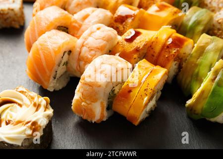 Set aus bunten Brötchen mit Garnelen, Lachs, Avocado, Käse auf einem schwarzen Steinteller, Nahaufnahme. Asiatische Küche, Sushi, Meeresfrüchte. Stockfoto