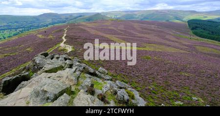 Ein Blick von der Spitze des Win Hill mit einem felsigen Vordergrund und einer lebhaften mauvenfarbenen Heidekraut in der Landschaft darunter. Stockfoto
