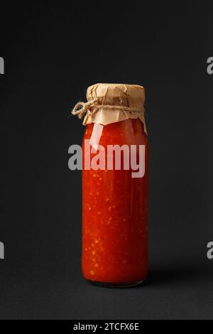 Heiße Sauce aus Chili, Paprika, Tomaten und Knoblauch in einem Glas, isoliert auf schwarzem Hintergrund. Kaukasische Soße, Adjika. Stockfoto