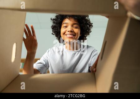 Ansicht von der Innenseite des Kartons. Afrikanisches Mädchen, das die Lieferung auspackt und in die Schachtel schaut. Frau öffnet Karton. Eine Frau bekommt ein Paket, das sich die gelieferten Waren ansieht. Zufriedenes positives Feedback des Kunden Stockfoto