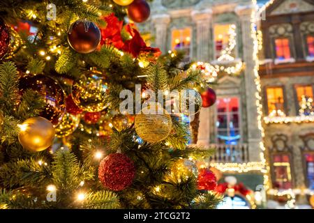 Nahaufnahme des festlich dekorierten Weihnachtsbaums im Freien mit bunten Kugeln auf einem schimmernden, glitzernden Feenhintergrund. Defokussierte Nachtstraße, Girlande Stockfoto