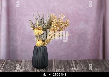 Trockene Blumen in schwarzer Keramikvase auf rosa Stoffhintergrund. Stockfoto