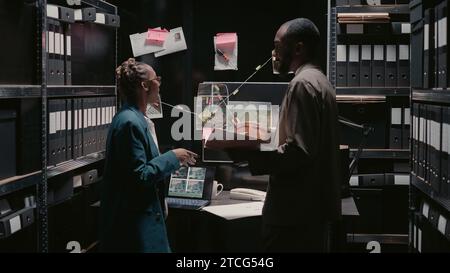 Polizeiagenten untersuchen Strafregister im Vorfallsraum und schauen sich verdächtige Fotos für Ermittlungen an. Ein junges Team von Detektiven analysiert Hinweise an Bord und Akten, Identifikation. Stockfoto