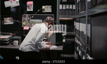 Eine Detektivin entdeckt Hinweise auf der Beweistafel, arbeitet an der Kriminalaufklärung im Archivraum. Weibliche Ermittlerin untersucht Überwachungsaufnahmen, sucht nach Einblicken und Details. Stockfoto