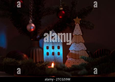 Brennende Kerze und hölzerne Weihnachtsdekoration mit Tannenzweigen auf dunklem Hintergrund. Weihnachts- oder Neujahrsgrußkarte. Stockfoto