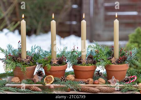 Adventsarrangements mit Kerzen in Terrakottatöpfen, die mit Kegeln und Nadelzweigen verziert sind Stockfoto