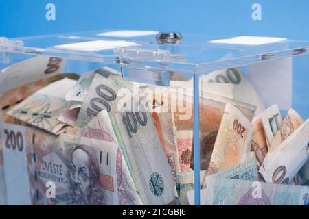 Wohltätigkeits- und Geldgeld CZK tschechische Kronen-Banknoten in einer transparenten Spendenbox für Geldspenden. Eine finanzielle Unterstützung, sammelt Geld. Der Akt des Gebens Stockfoto