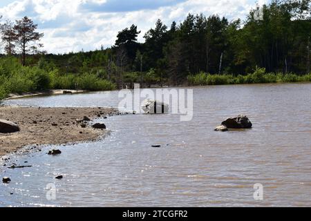 Die Landschaft am See mit einigen Felsbrocken im Wasser neben dem Strand und Sonnenlicht reflektiert auf der Wasseroberfläche Stockfoto