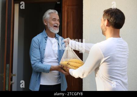 Mann mit Netztüte mit Produkten, die seinem Seniorennachbarn im Freien helfen Stockfoto