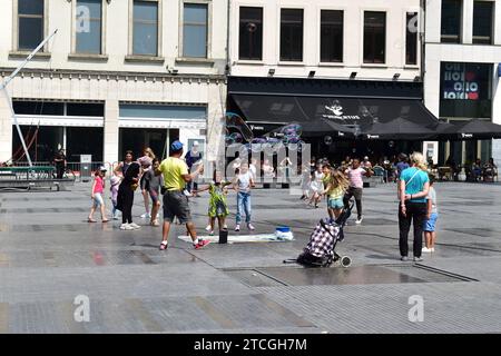 Mann in gelbem T-Shirt, der große Seifenblasen erzeugt, um kleine Kinder auf dem Munt (Punt) Platz im Stadtzentrum von Brüssel zu unterhalten Stockfoto