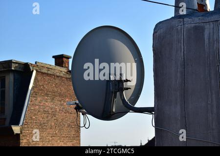 Rückansicht einer grauen Satellitenschüssel mit Ziegelbau und blauem Himmel im Hintergrund Stockfoto