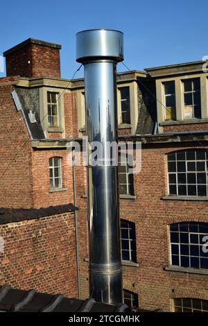 Nahaufnahme einer Edelstahl-Chrom-Metall-Lüftungsöffnung, die als Schornstein auf einem Dach mit Ziegelbau im Hintergrund verwendet wird Stockfoto