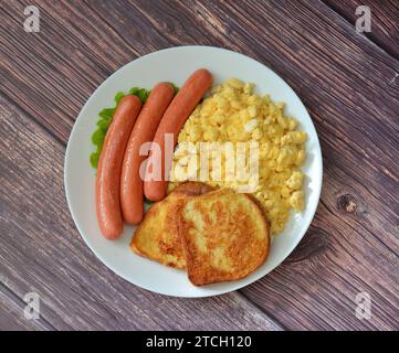 Gekochte Würstchen, Rührei und Brottoast mit Ei auf einem Holztisch. Draufsicht, flach. Stockfoto