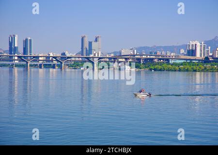 Ein kleines Schnellboot gleitet über den weitläufigen Han River und bietet im Hintergrund einen malerischen Blick auf Seoul's Yongsan Viertel. Stockfoto