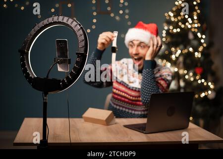 Arabischer Mann im Weihnachtsmann, der Videos mit der Telefonkamera aufnimmt, während er die Box mit einer neuen Smart Watch auspackt. Männlicher Influencer teilt mit Abonnenten sein positives Stockfoto