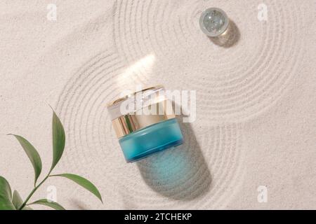 Blick von oben auf ein luxuriöses Lotionsglas auf einem glatten Sandgrund mit Glasmarmor, mit grünen Blättern in der Ecke des Rahmens. Kosmetisches Mock Stockfoto