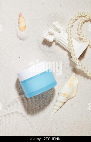 Ein unbeschriftetes Kosmetikglas, eine Perlenschnur, Muscheln und Ornamente auf einem glatten sandigen Hintergrund. Leeres Etikett für Schriftdesign. Branding und A Stockfoto